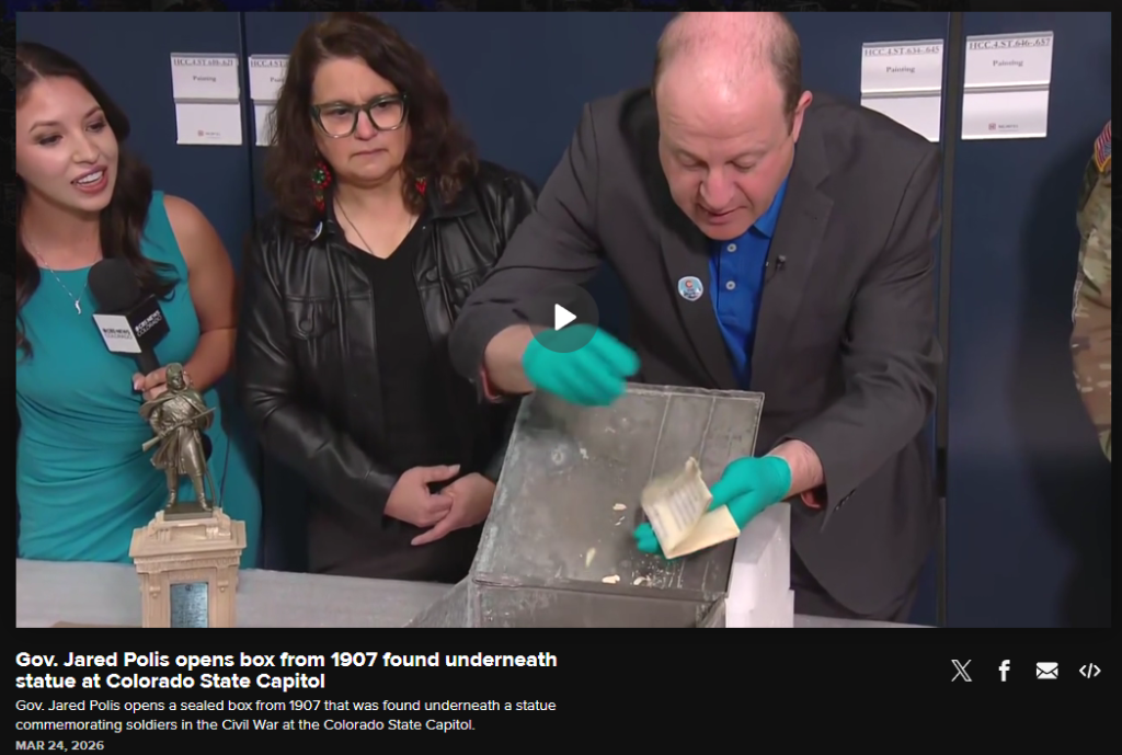 History Colorado staff and Colorado Governor Jared Polis pulling historic documents from the time capsule box inside a collections room as the paper disintegrates in his hands.